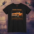 Black t-shirt with orange classic car graphic and text on a wooden surface with sunglasses and keys.
