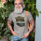 Man wearing a gray t-shirt with a classic car graphic and text, standing outdoors with greenery in the background.