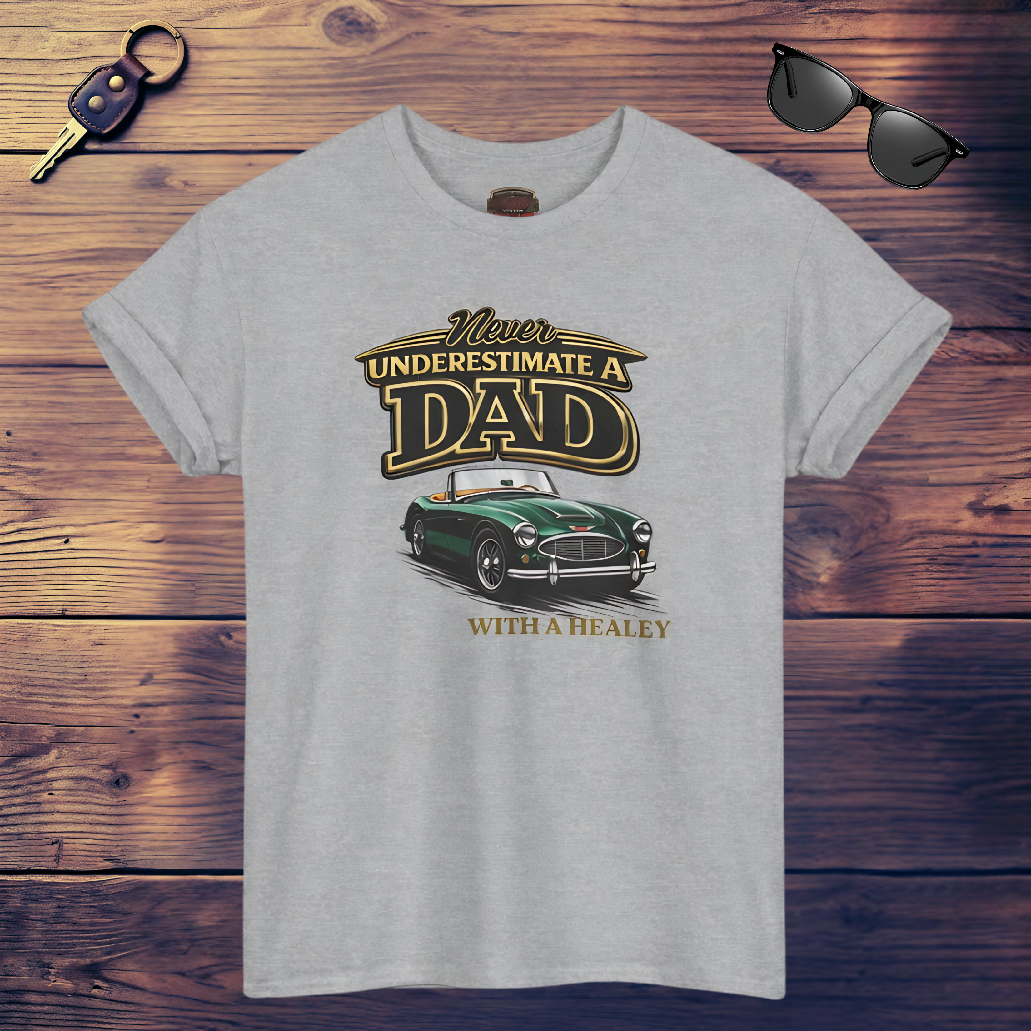 Sport gray t-shirt with a graphic design of a car and text on a wooden surface with sunglasses and a key.