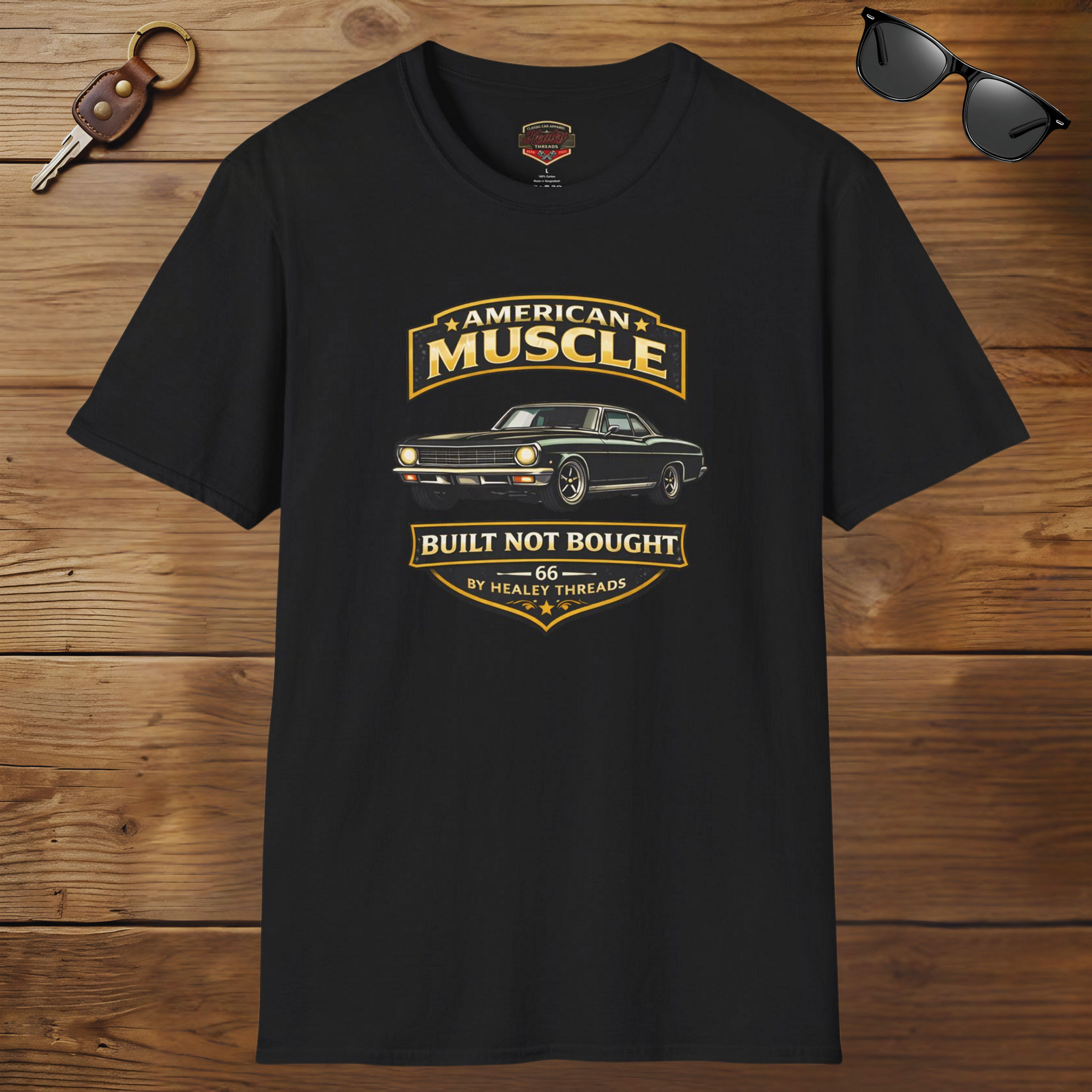 Black t-shirt with 'American Muscle' car graphic design on a wooden surface with sunglasses and keychain.