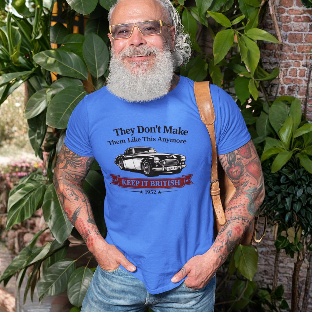 Man wearing a royal blue t-shirt with a Healey graphic and text, standing outdoors among greenery.
