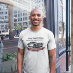 Man wearing a gray t-shirt with a graphic design of a classic car and text, standing in an urban setting.