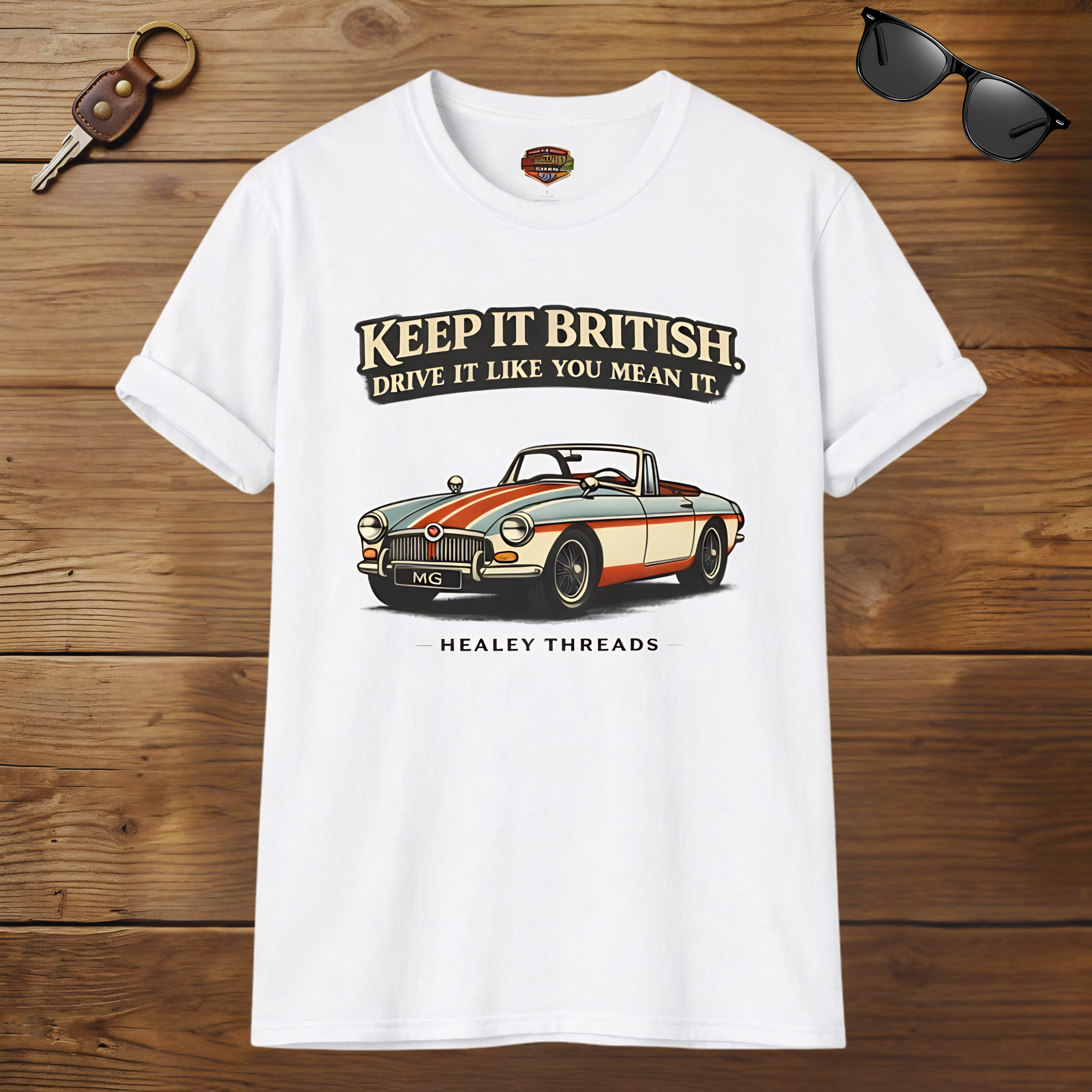 White t-shirt with MG car graphic and text on a wooden surface, accompanied by sunglasses and a key.