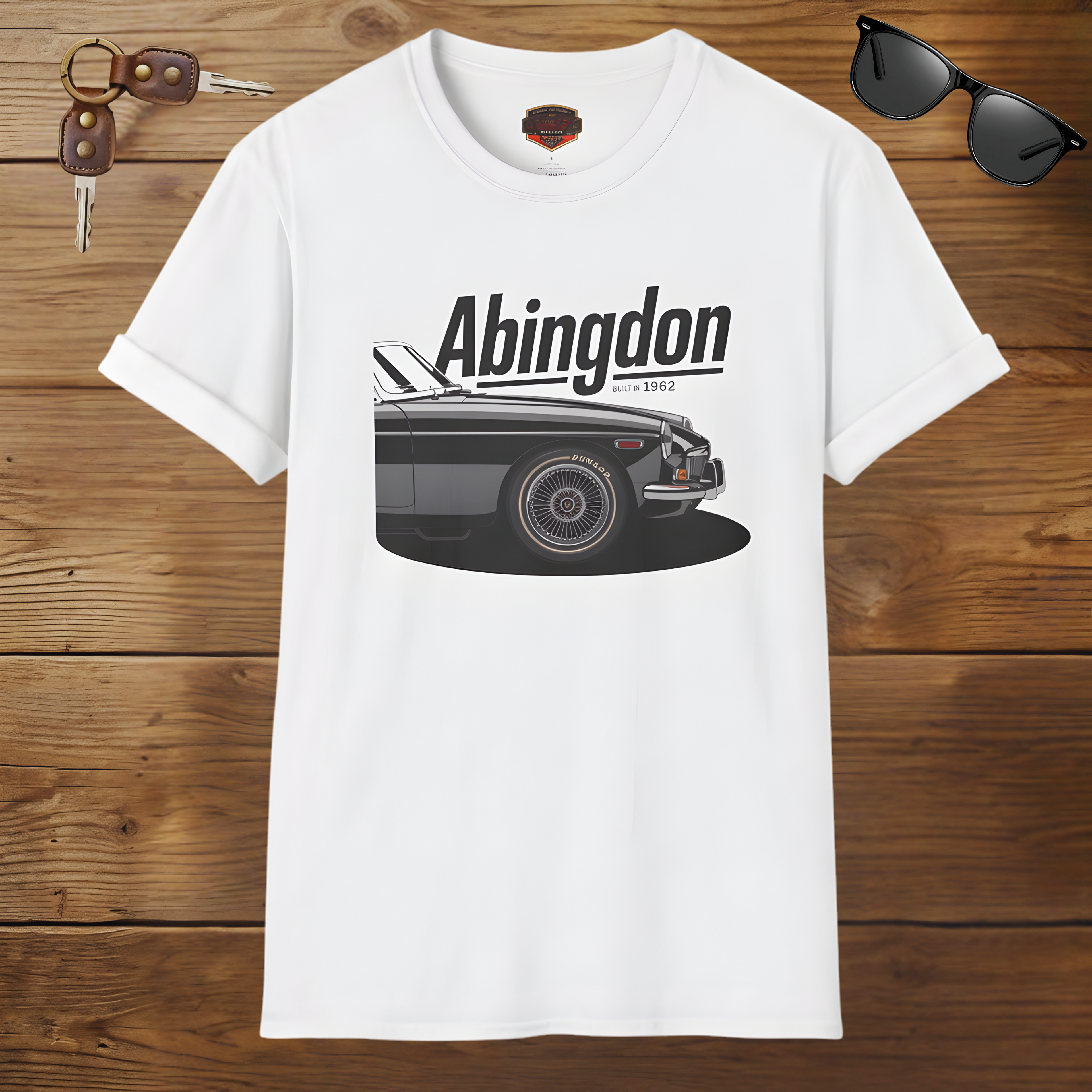 White t-shirt with a classic car graphic and 'Abingdon' text on a wooden surface with sunglasses and keys.