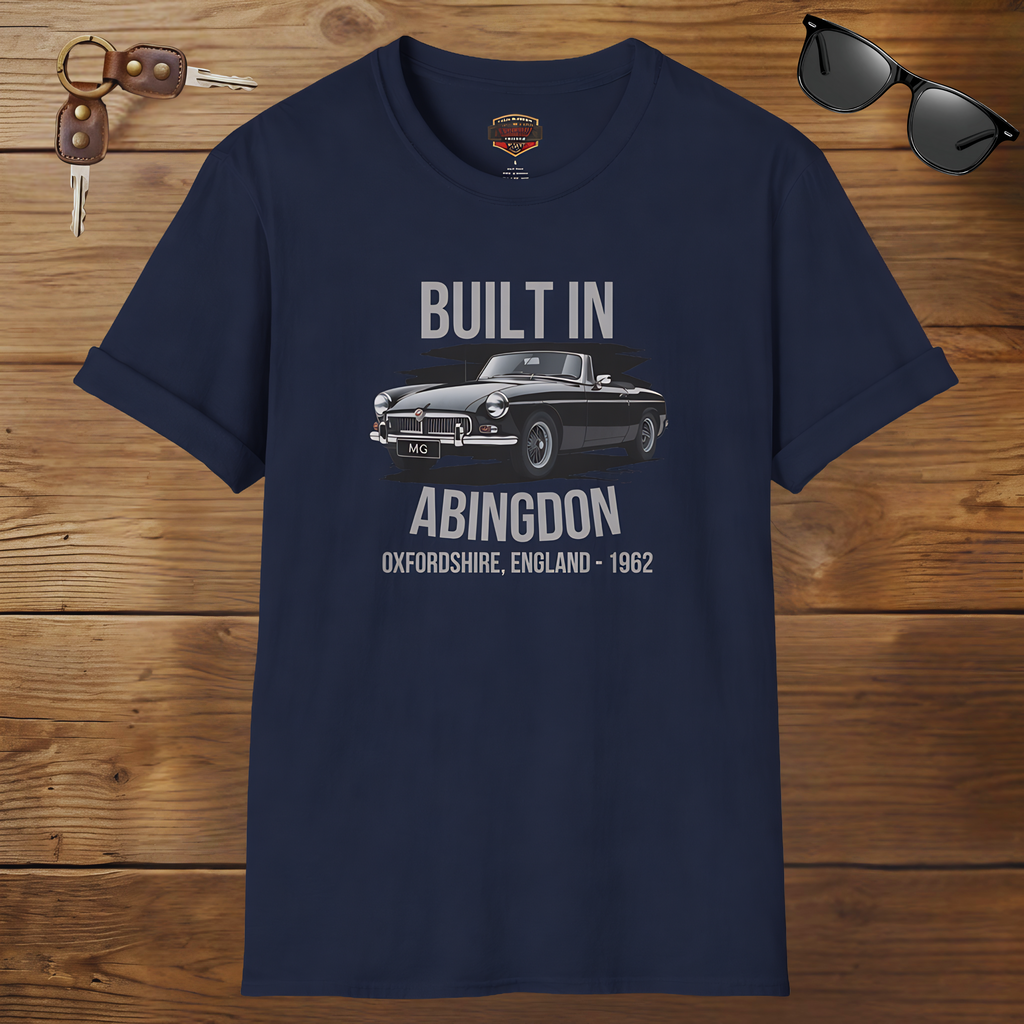 Navy blue t-shirt with car graphic and text on a wooden surface with sunglasses and keys.