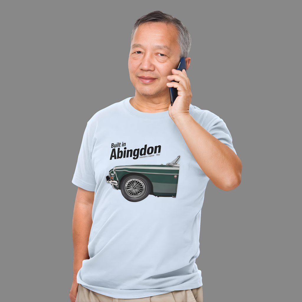 Man wearing a light blue t-shirt with a classic car graphic and text, talking on a phone against a gray background