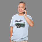 Man wearing a light blue t-shirt with a classic car graphic and text, talking on a phone against a gray background