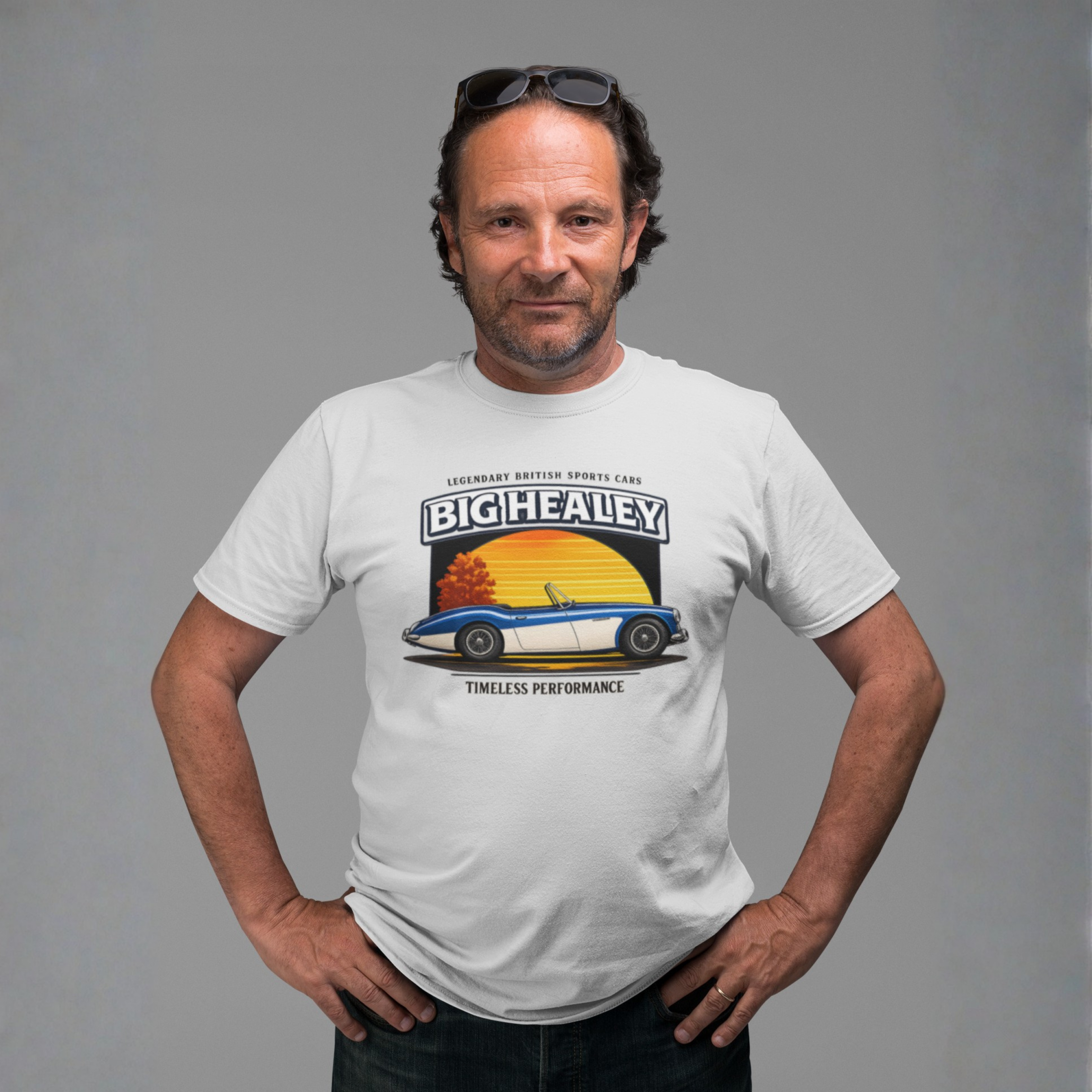 Man wearing a Big Healey graphic white colored t-shirt featuring a blue and white Austin Healey roadster with retro sunset artwork and vintage British sports car on a gray background