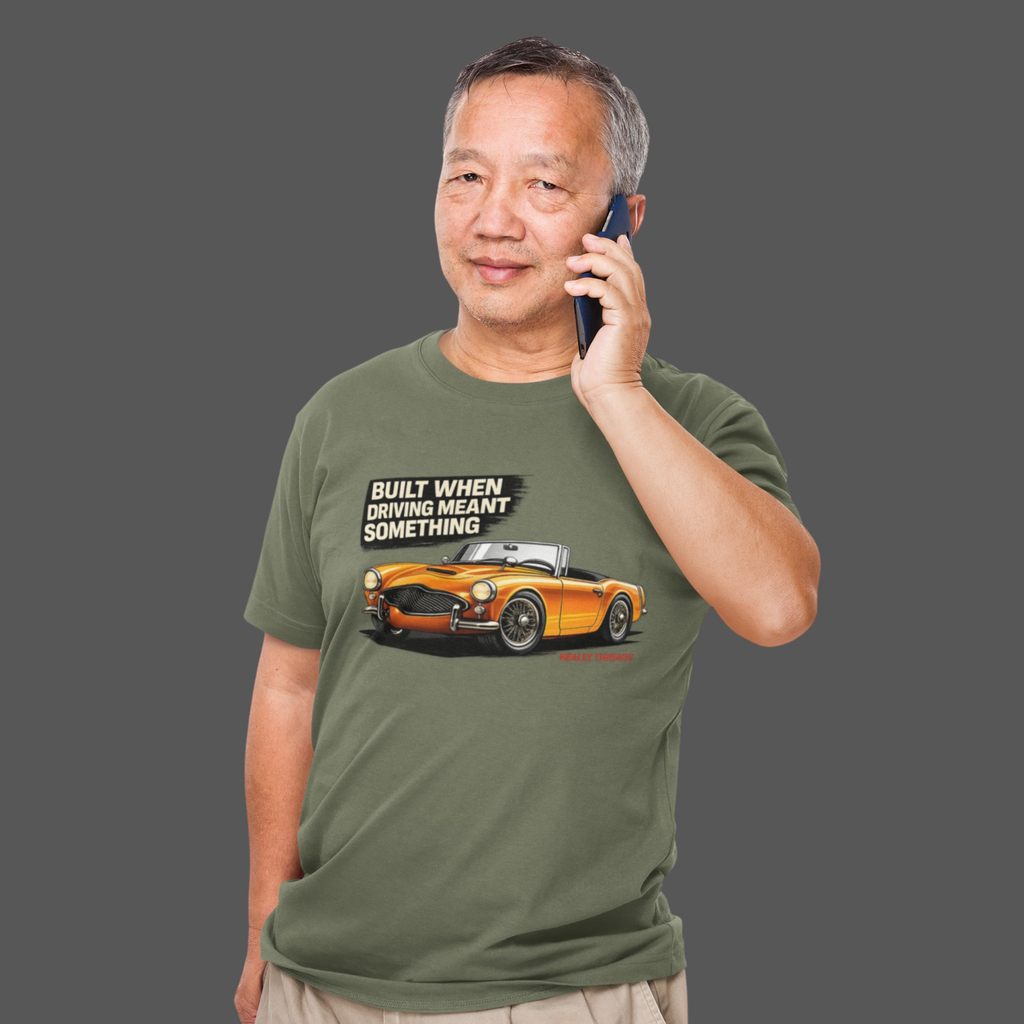 Man wearing a military green t-shirt with a car graphic and text, talking on a phone.