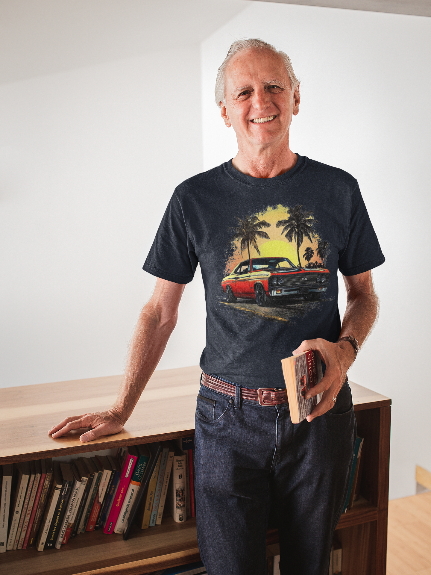 Man wearing a navy t-shirt with a classic car and palm tree design, standing in a room with a bookshelf.