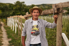 Man wearing a checkered shirt with a graphic classic car design, standing next to a wooden fence in a rural setting.
