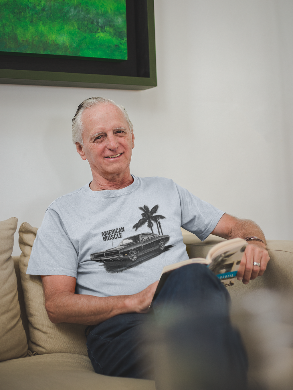 Man sitting on a couch wearing a gray t-shirt with a graphic design, with a television in the background.