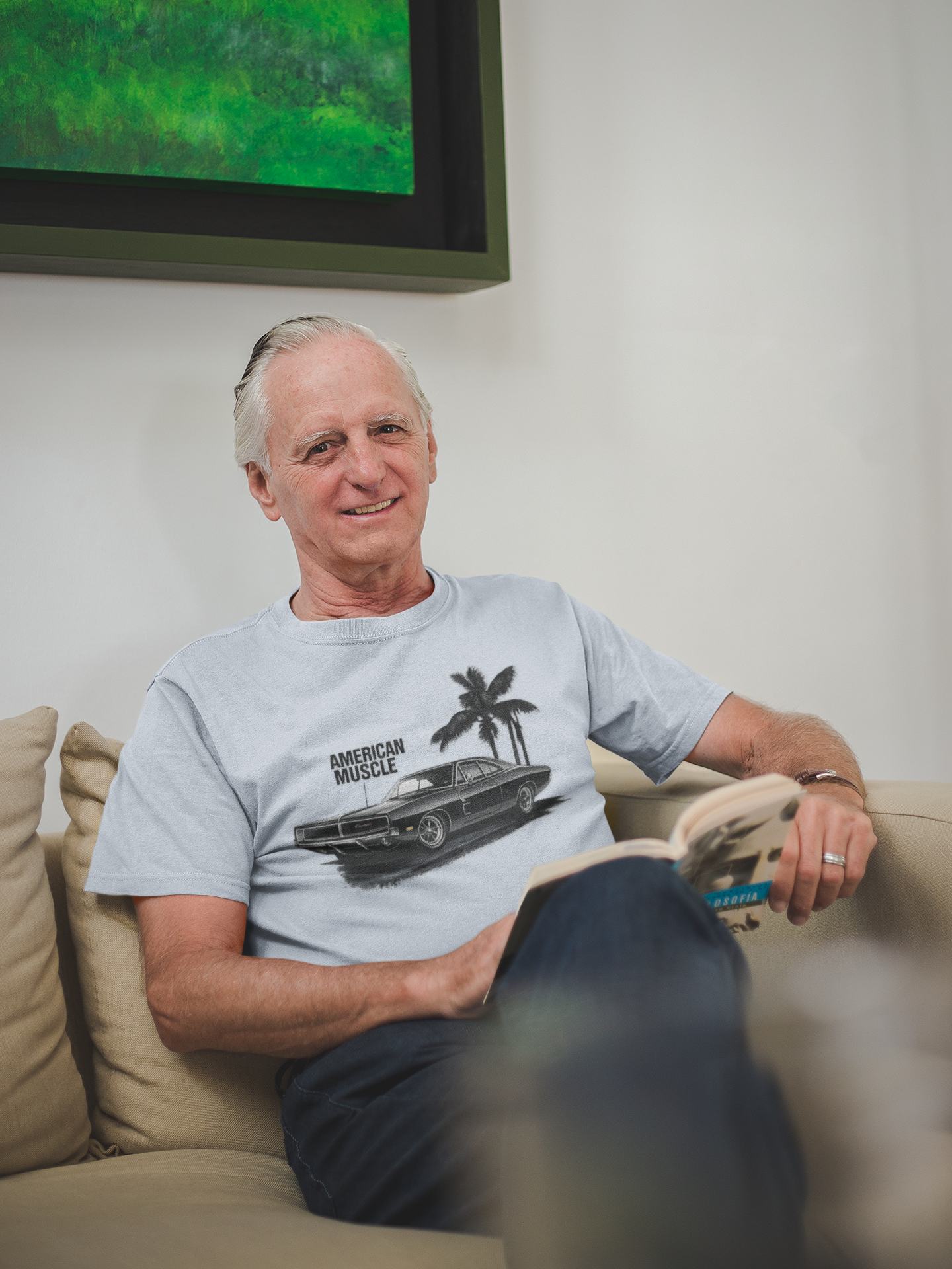 Man sitting on a couch wearing a gray t-shirt with a graphic design, with a television in the background.