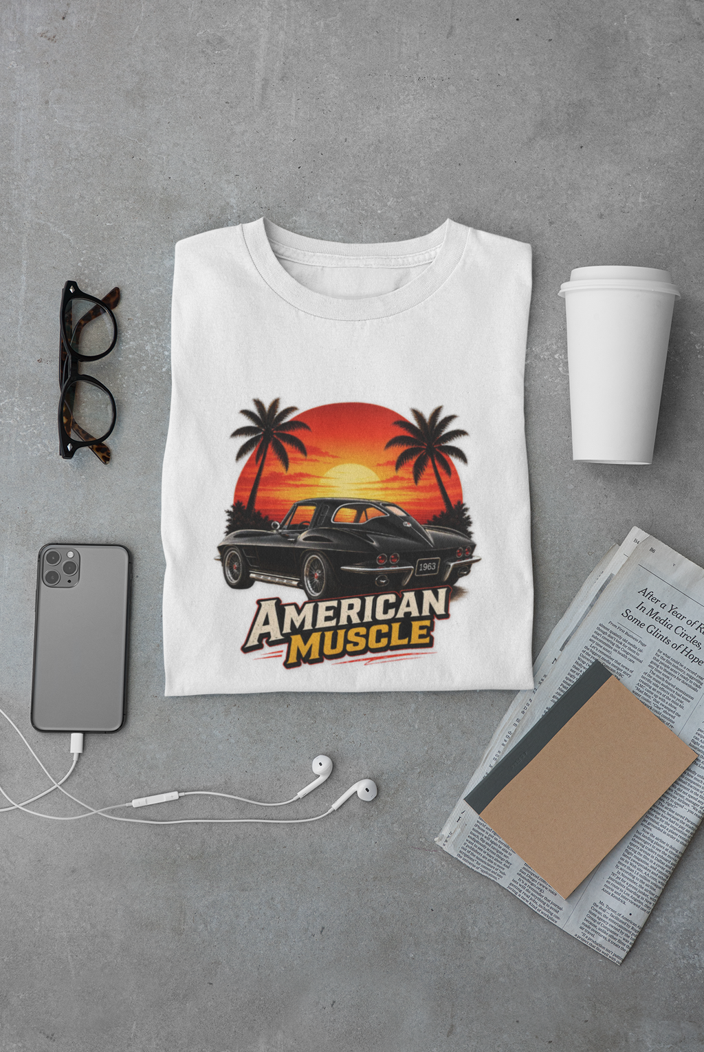 White t-shirt with 'American Muscle' graphic on a gray surface with phone, cup, and glasses.