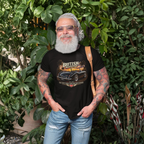 Man wearing a black t-shirt with a car graphic and text, standing outdoors among greenery.