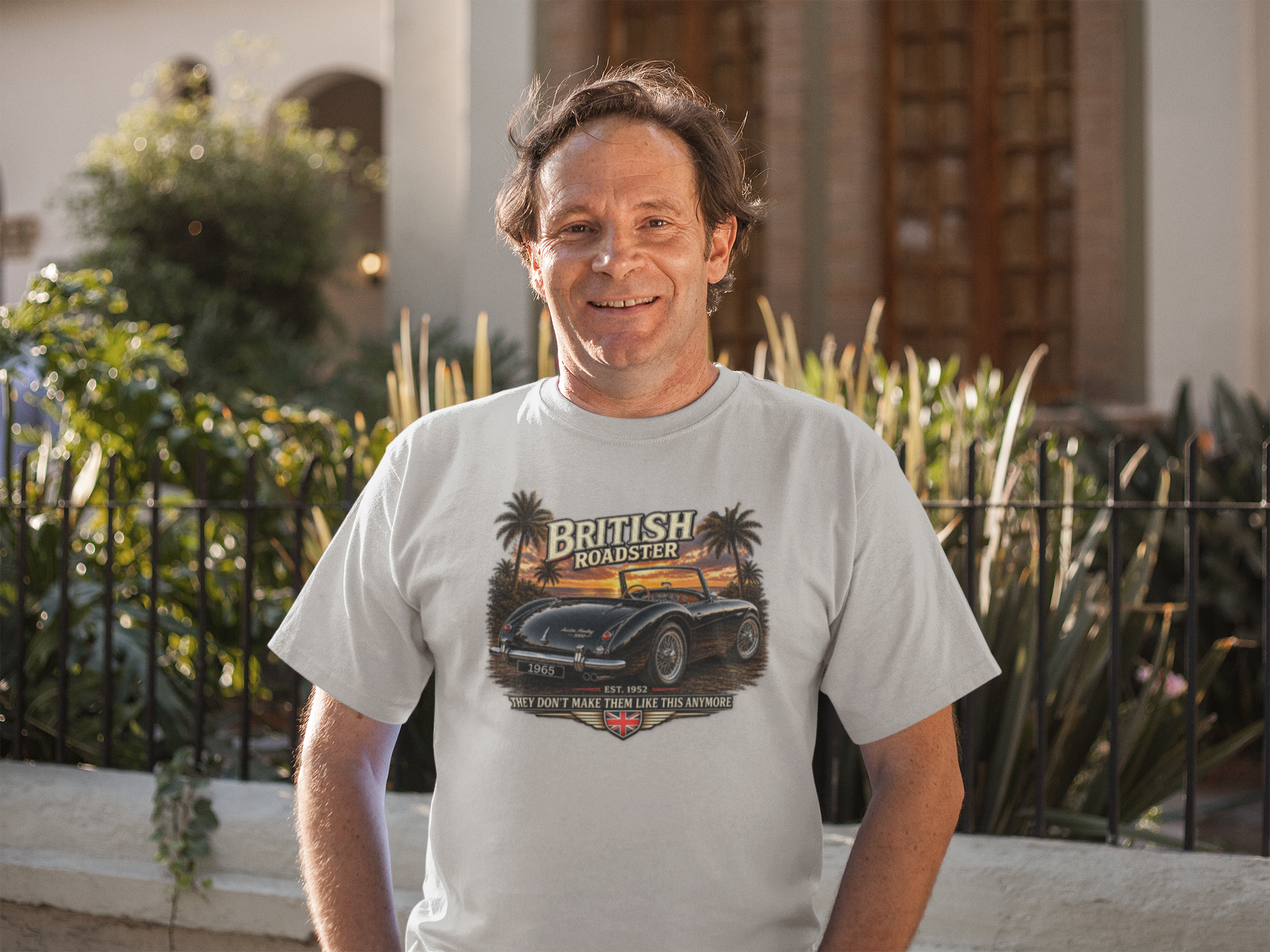 Man wearing a t-shirt with a graphic design of a vintage car and text, standing outdoors.