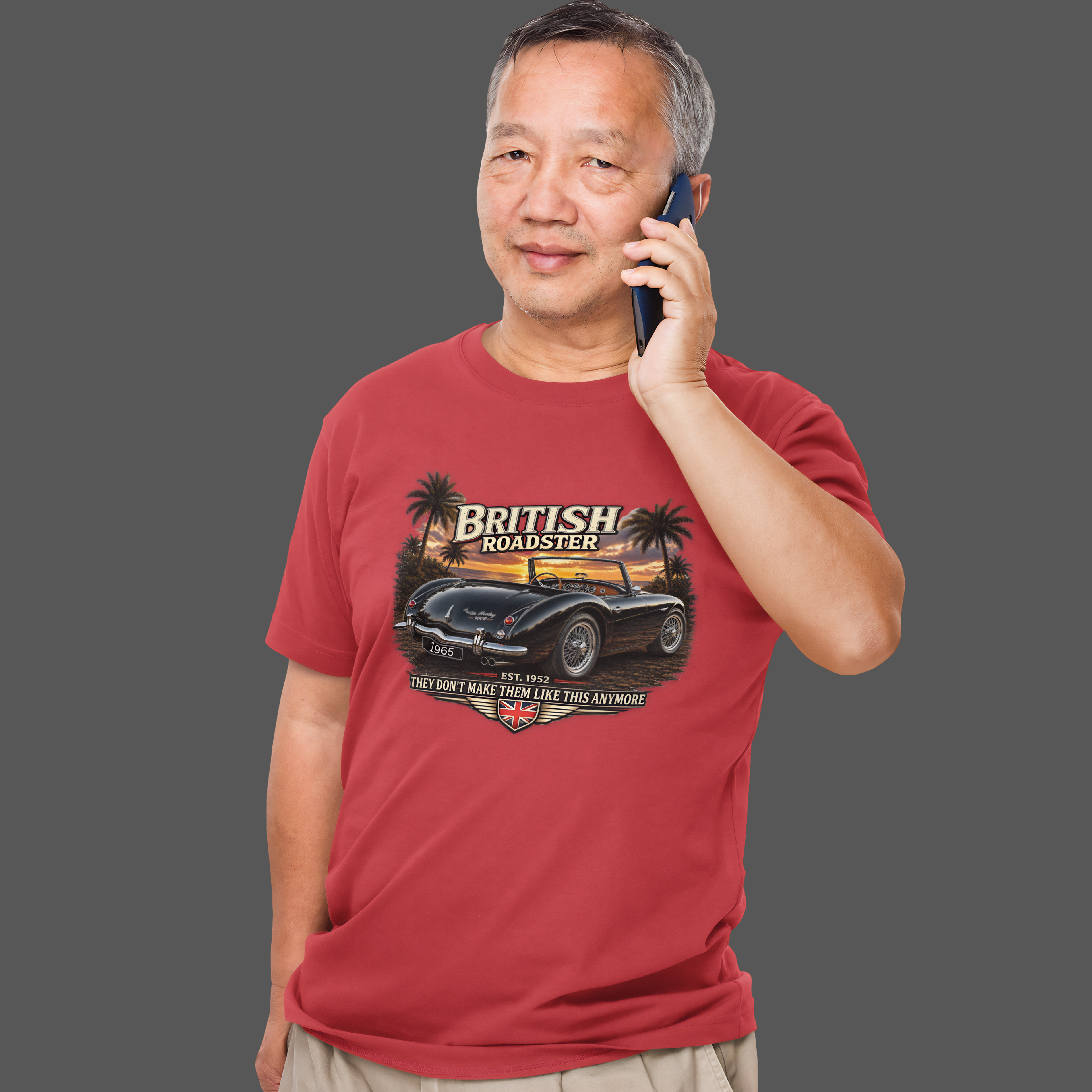 Man wearing a red t-shirt with a graphic design of a British roadster car, talking on a phone.