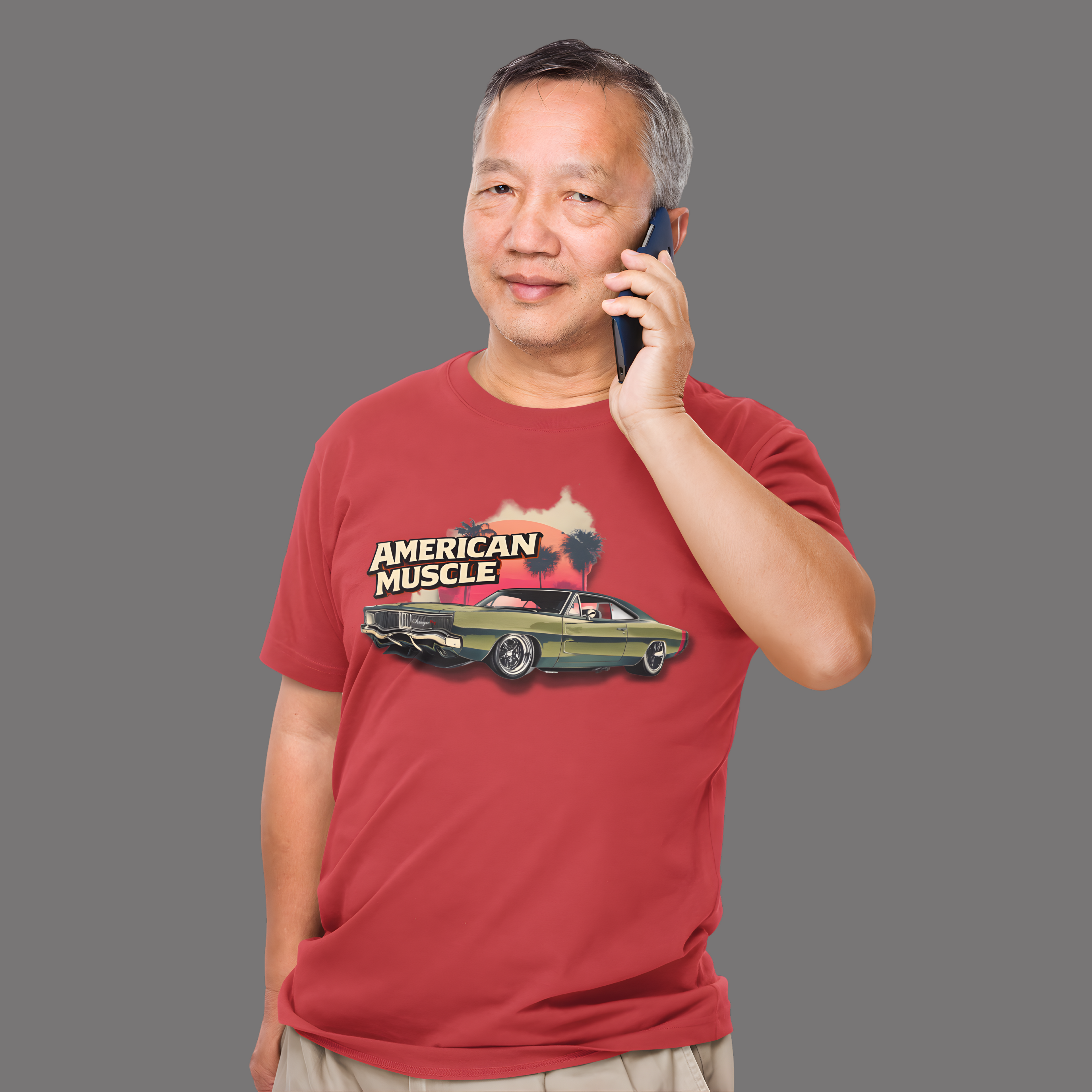 Man wearing a red t-shirt with 'American Muscle' graphic, talking on a phone against a gray background