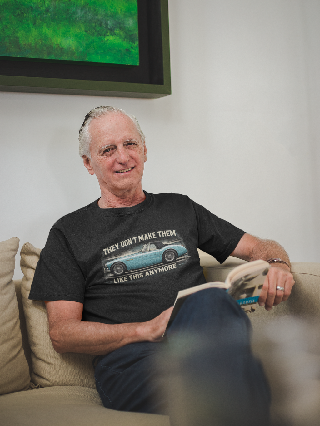 Man sitting on a couch wearing a black t-shirt with a graphic Healey design.