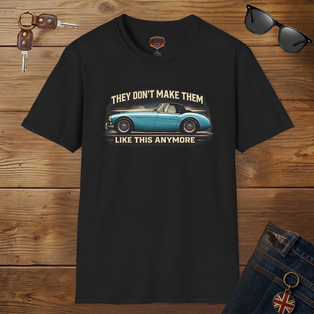 Black t-shirt with a graphic of a classic car and text on a wooden surface with sunglasses and keys.