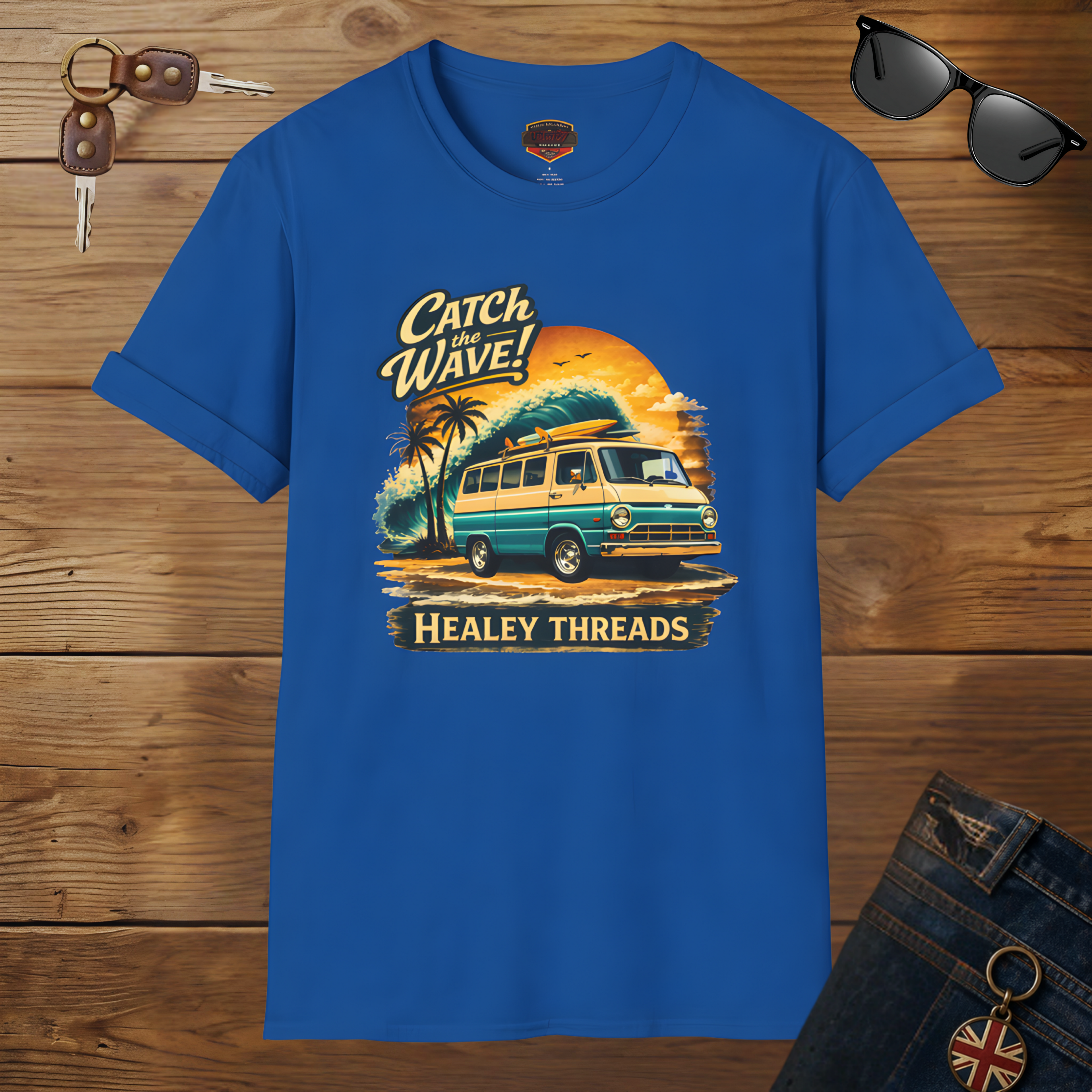 Royal blue t-shirt with a graphic design of a van and text 'Catch the Wave! Healey Threads' on a wooden surface.