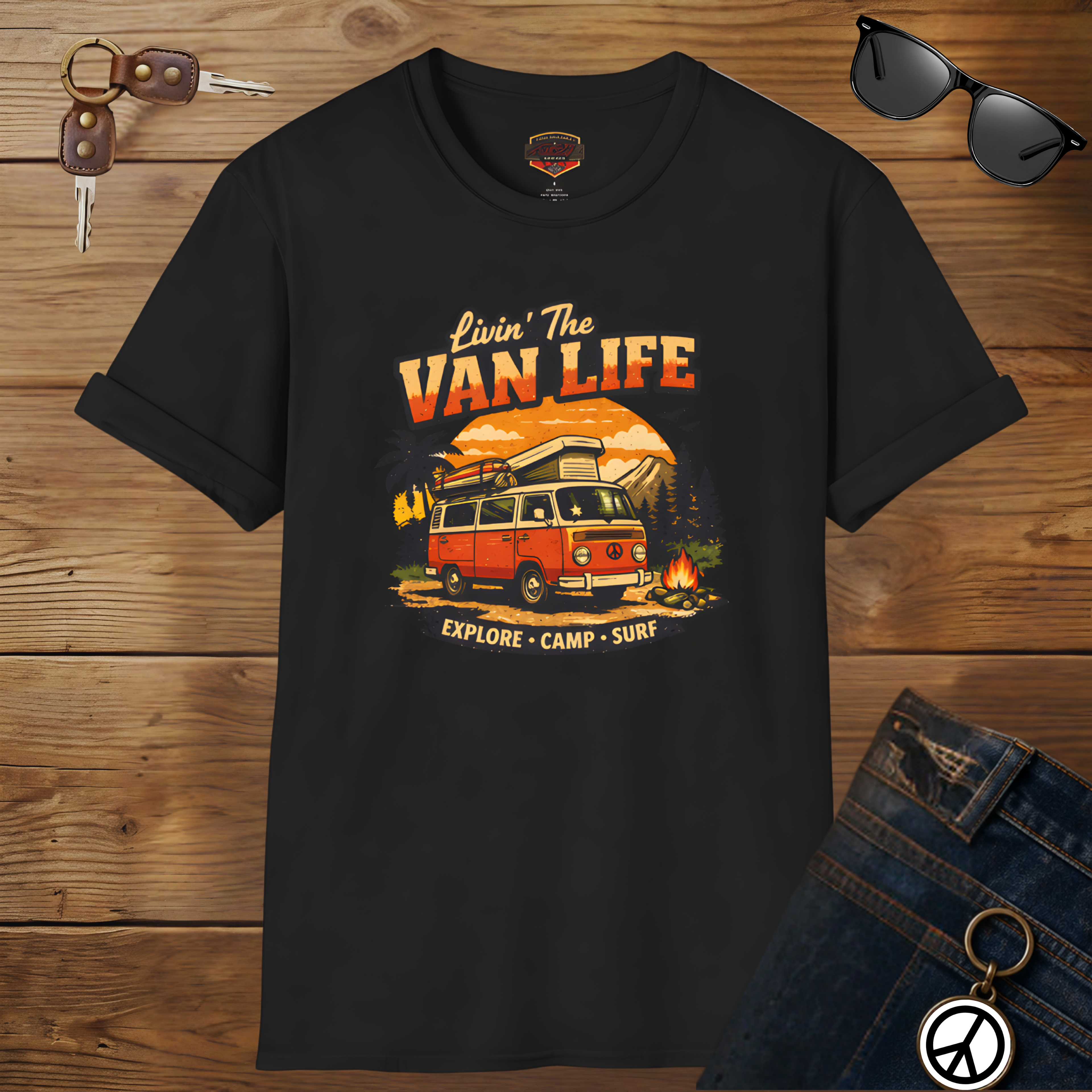 Black t-shirt with 'Livin' The Van Life' graphic design on a wooden surface with sunglasses and jeans.