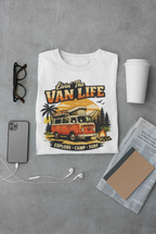 Folded white t-shirt with 'Livin' The Van Life' graphic on a gray surface with accessories.