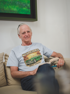 Man sitting on a couch wearing a gray t-shirt with a classic car graphic design.