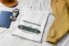 White t-shirt with classic car graphic and text on a white surface with accessories.