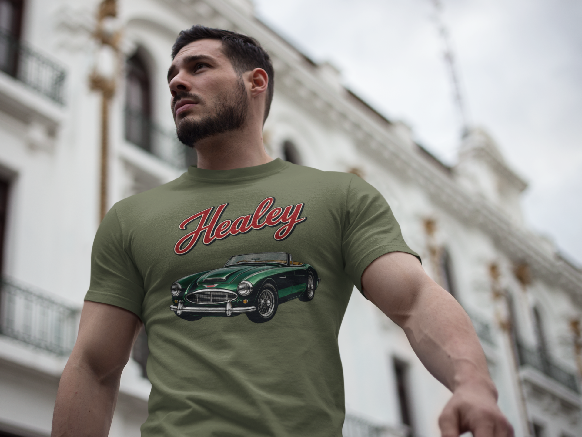 Man wearing a military green t-shirt with a classic Healey car design in an urban setting