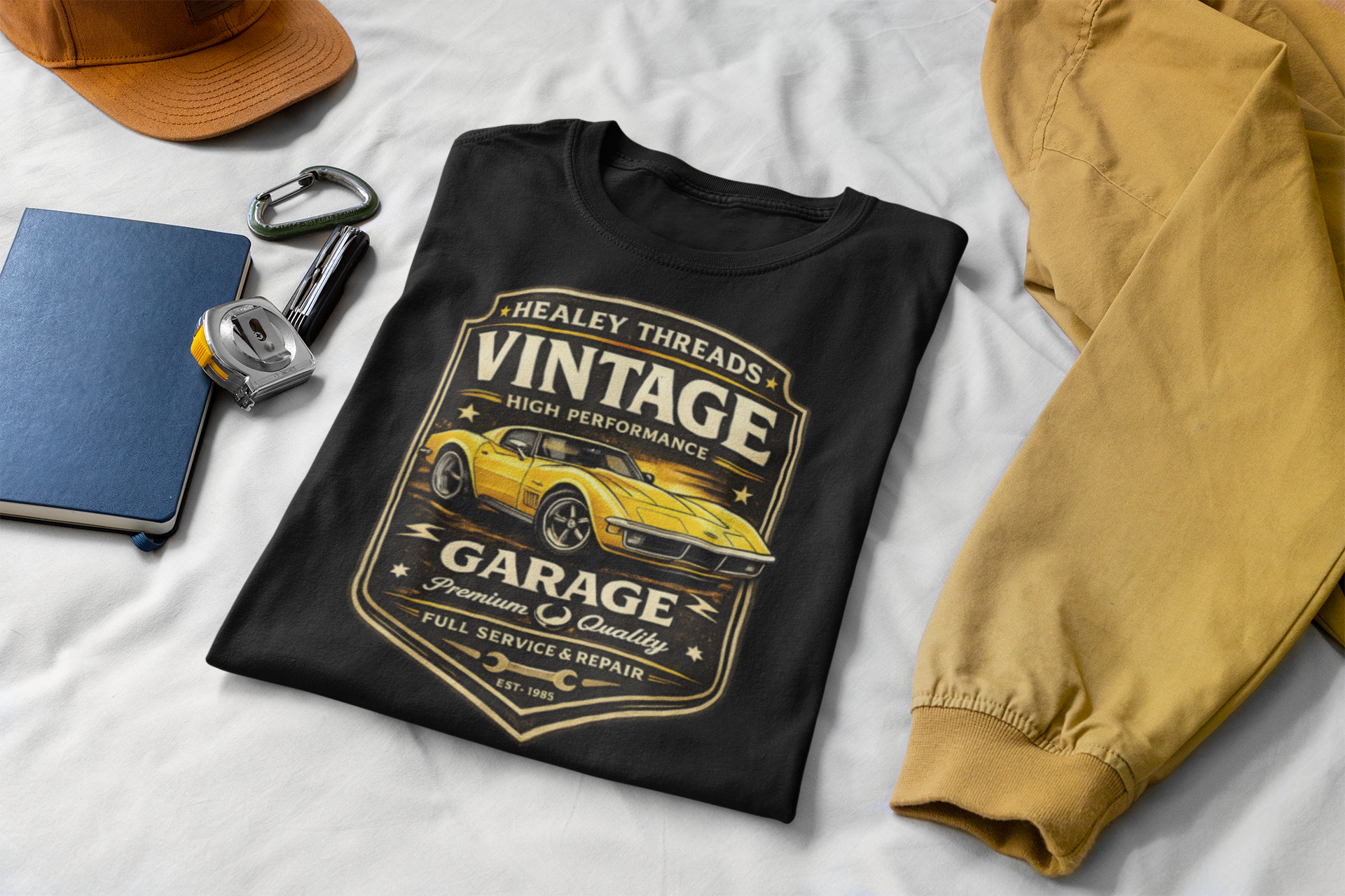 Black t-shirt with vintage classic car graphic on a white surface with accessories.