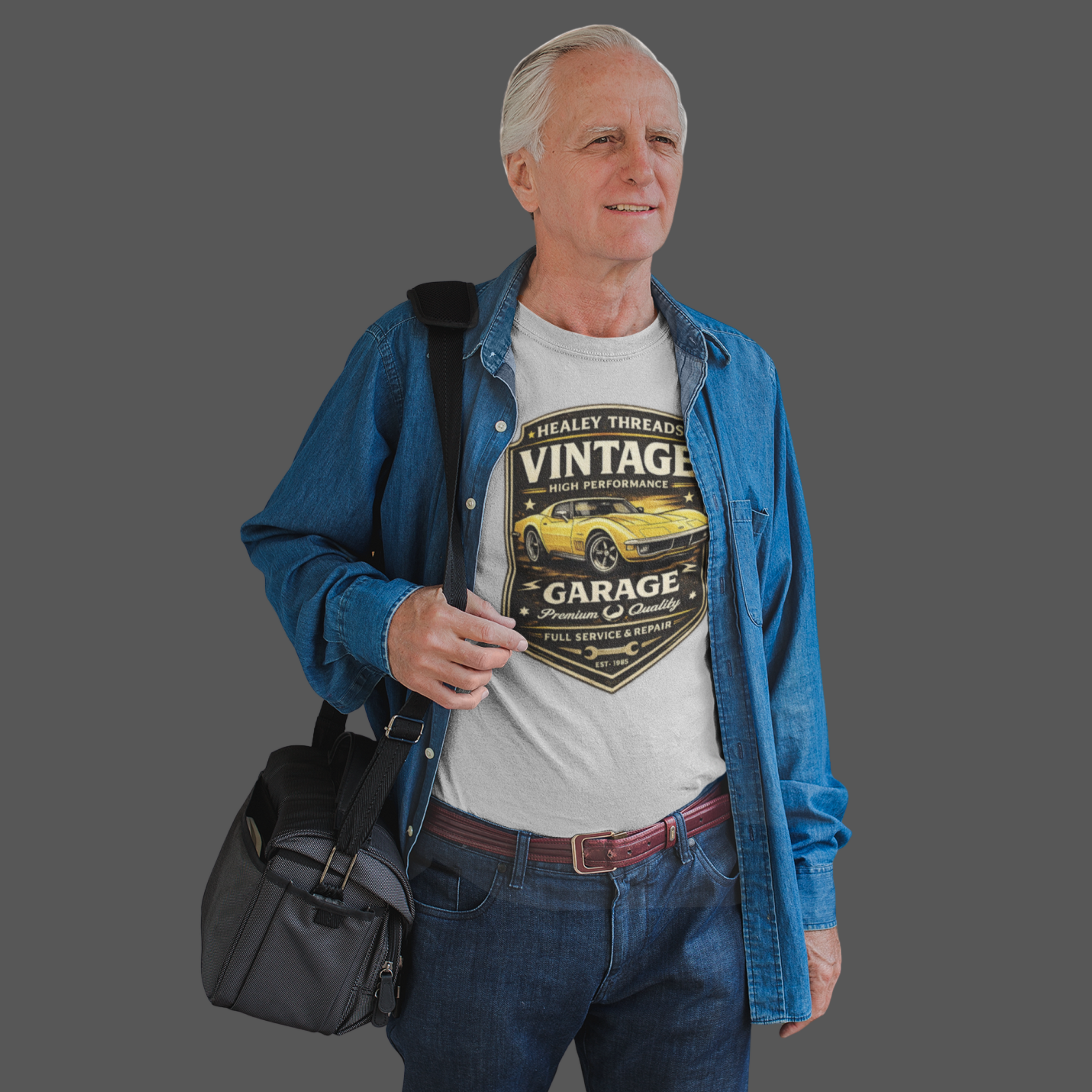 Man wearing a white t-shirt with a vintage classic car graphic and a blue jacket, holding a black bag.