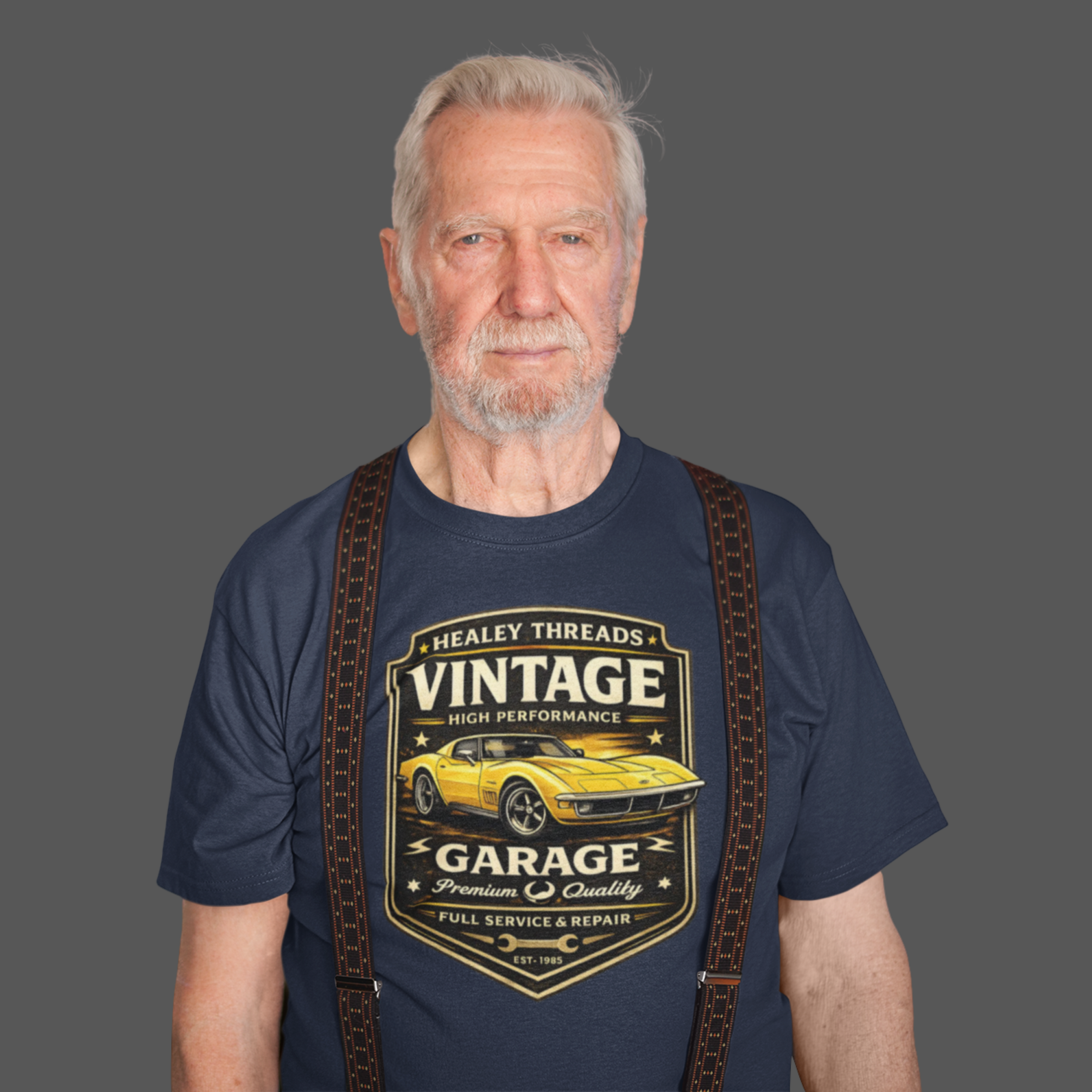 Man wearing a navy blue t-shirt with a vintage classic car graphic and suspenders on a gray background