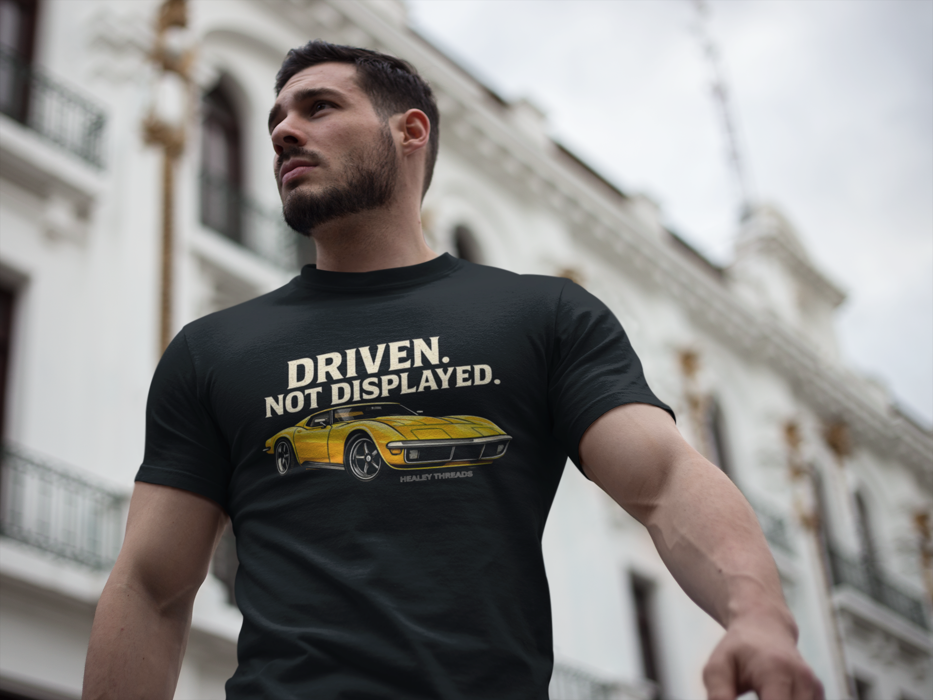 Man wearing a black t-shirt with a yellow muscle car graphic and text in an urban setting