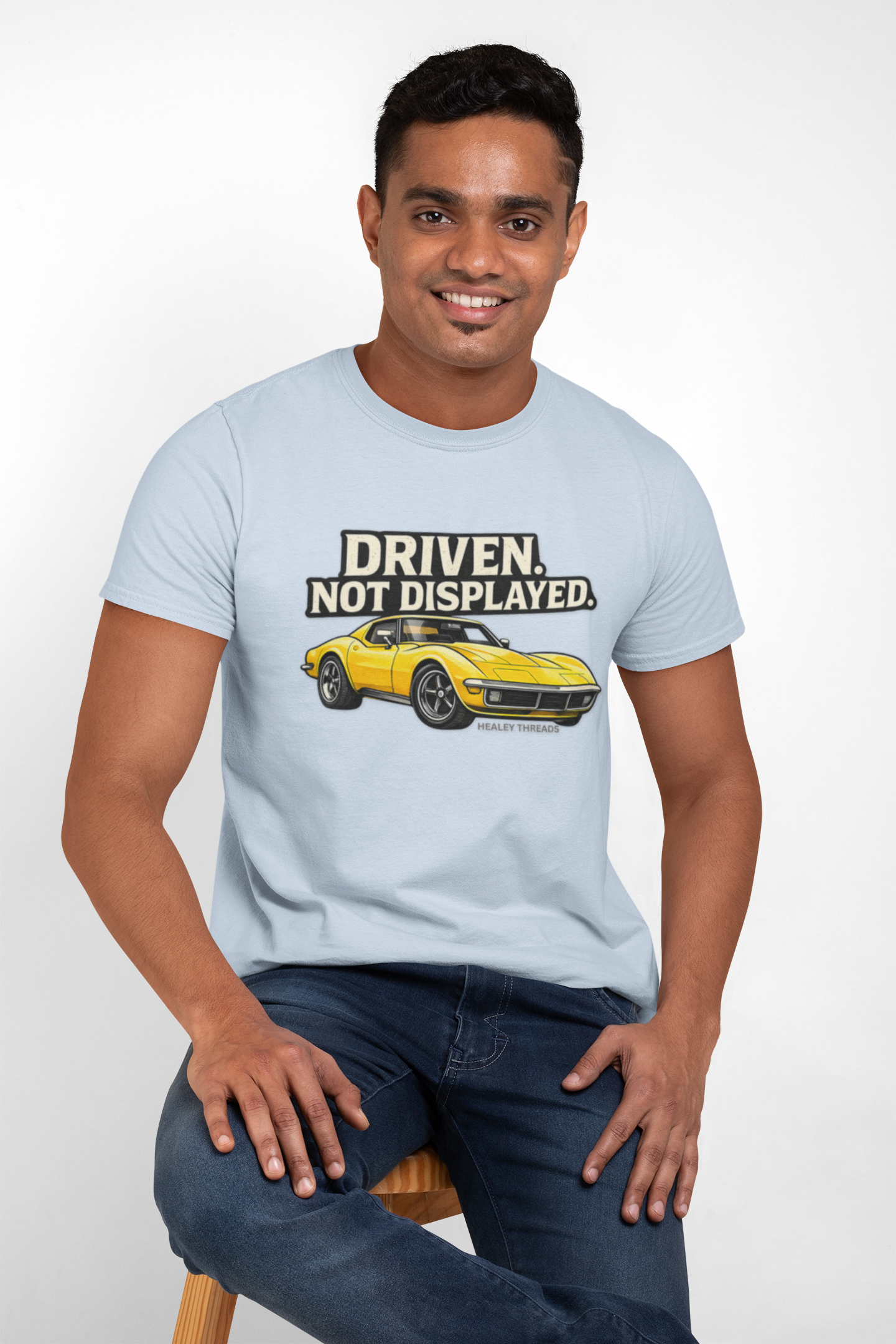 Man wearing a light blue t-shirt with a muscle car graphic and text, sitting on a white background