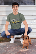 Man sitting on steps with a dachshund wearing a military green t-shirt with text and a muscle car graphic.