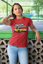 Woman wearing a red t-shirt with a graphic muscle car and text, standing against a green metal fence.