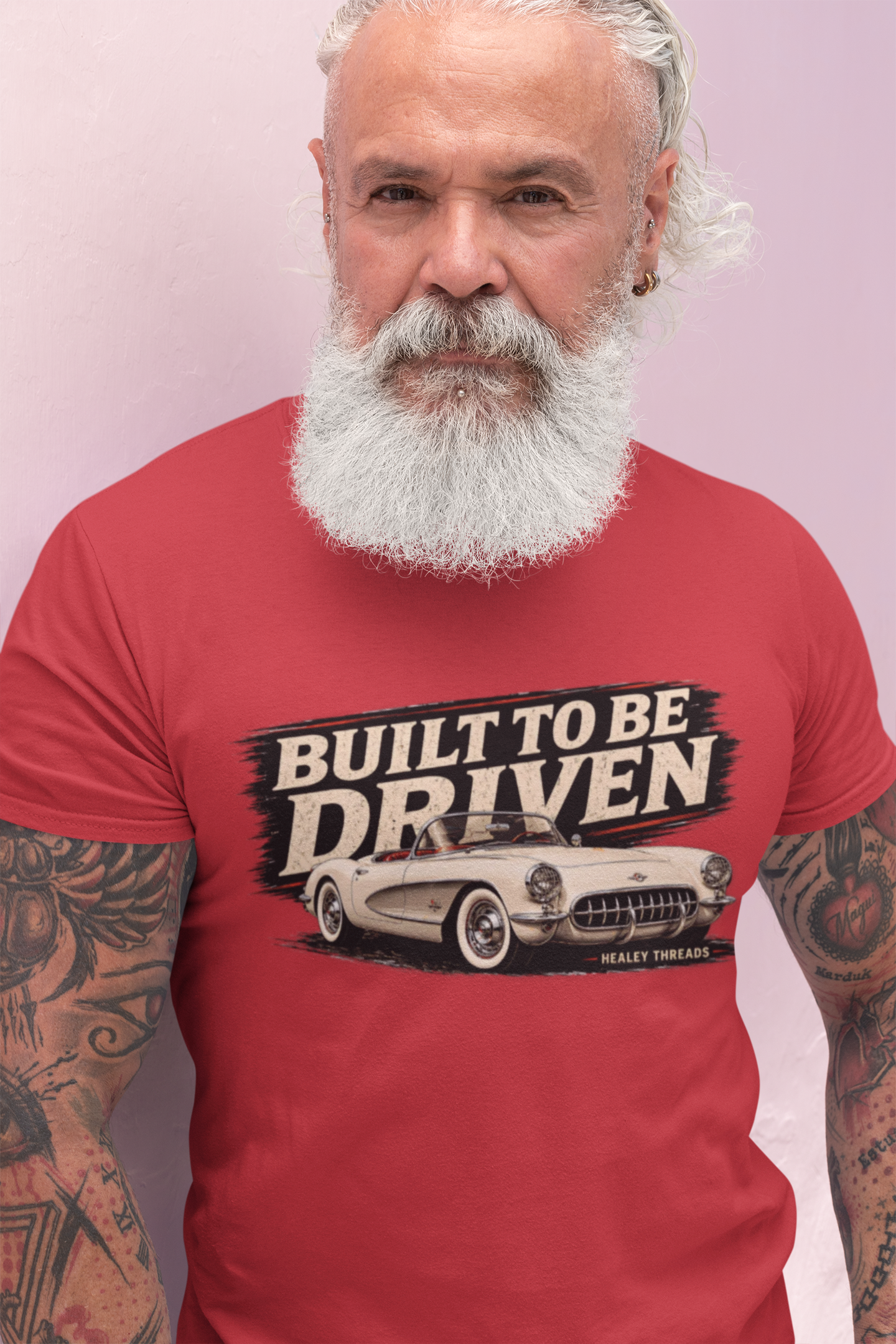 Man wearing a red t-shirt with a graphic built to be driven design and text, standing against a light purple background.