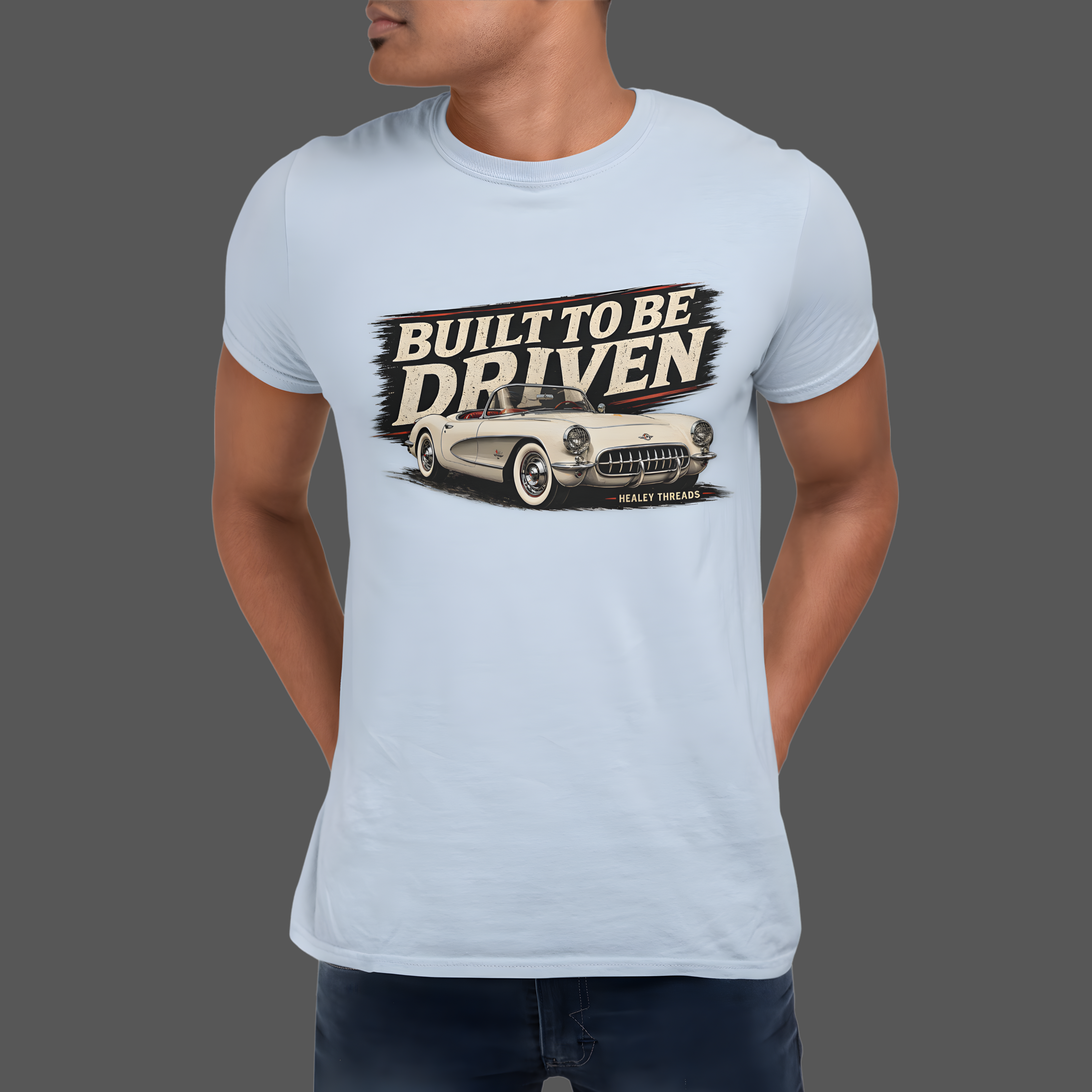 Light blue t-shirt with a graphic of a classic car and text 'Built to be Driven' worn by a person on a gray background