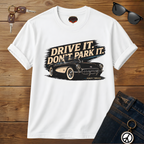 White t-shirt with car graphic and text 'Drive it. Don't park it.' on a wooden surface.