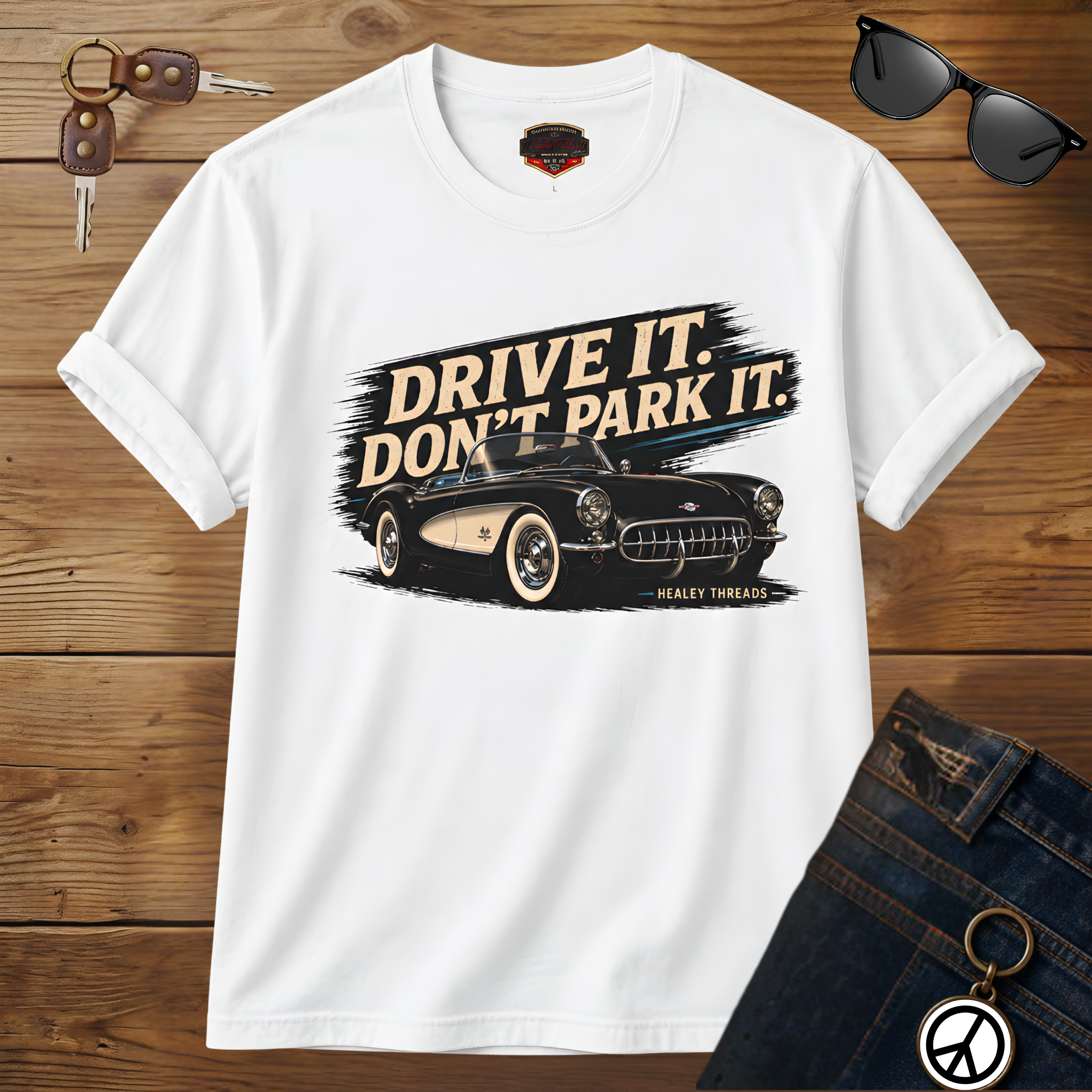 White t-shirt with car graphic and text 'Drive it. Don't park it.' on a wooden surface.