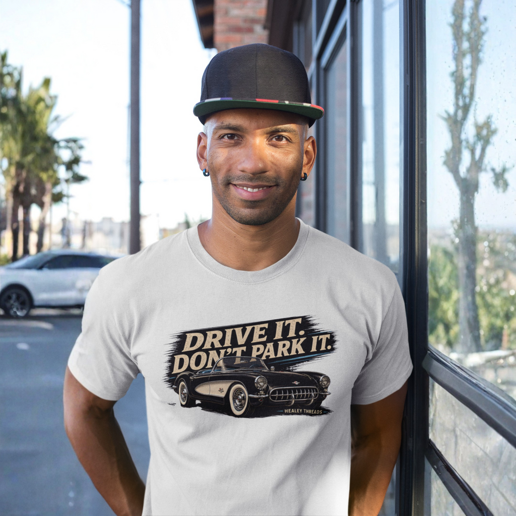 Man wearing a t-shirt with 'Drive It, Don't Park It' graphic and cap, standing outdoors.