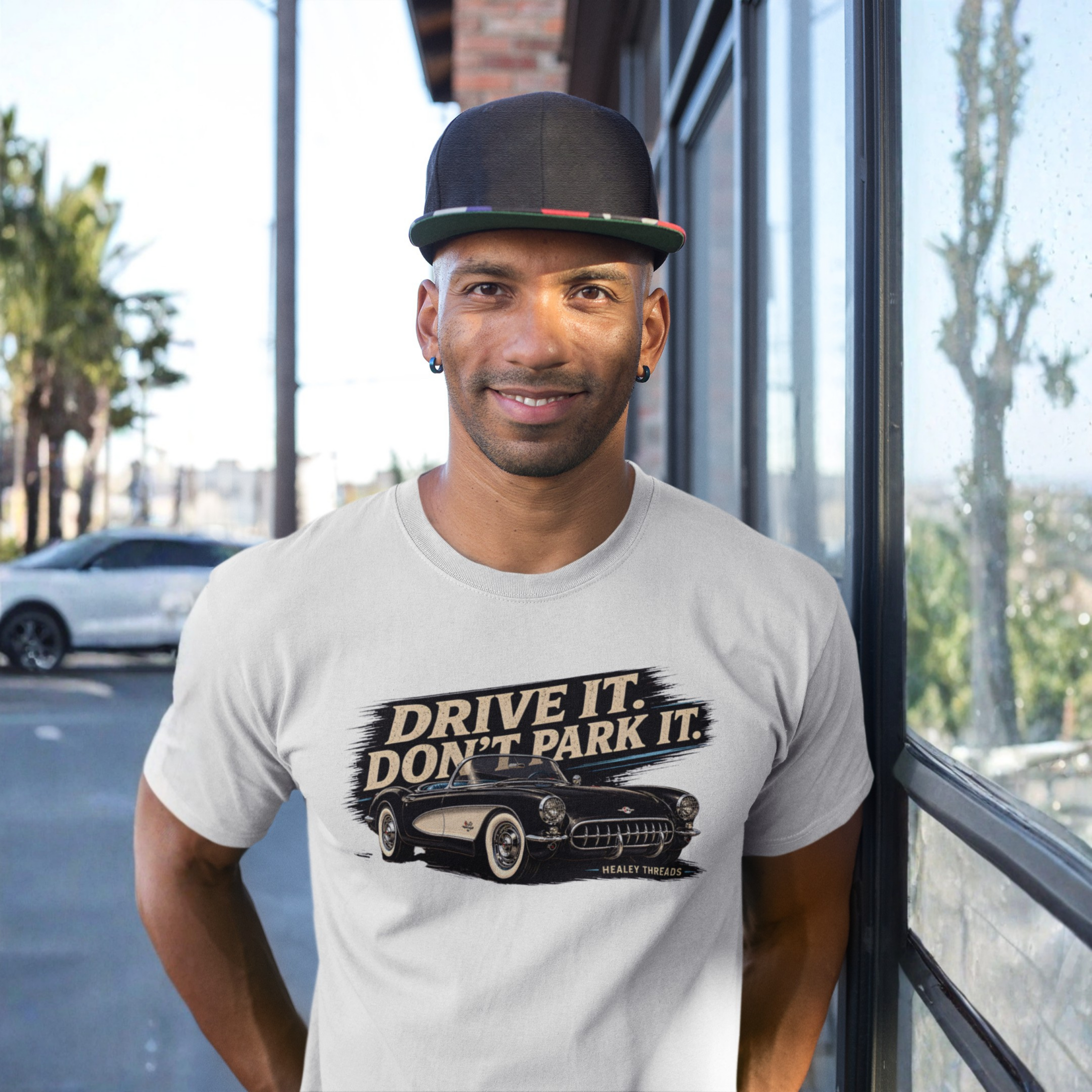 Man wearing a t-shirt with 'Drive It, Don't Park It' graphic and cap, standing outdoors.