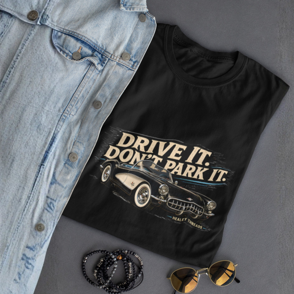 Black t-shirt with 'Drive It. Don't Park It.' graphic on a gray surface with denim jacket, sunglasses, and necklace.