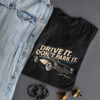 Black t-shirt with 'Drive It. Don't Park It.' graphic on a gray surface with denim jacket, sunglasses, and necklace.