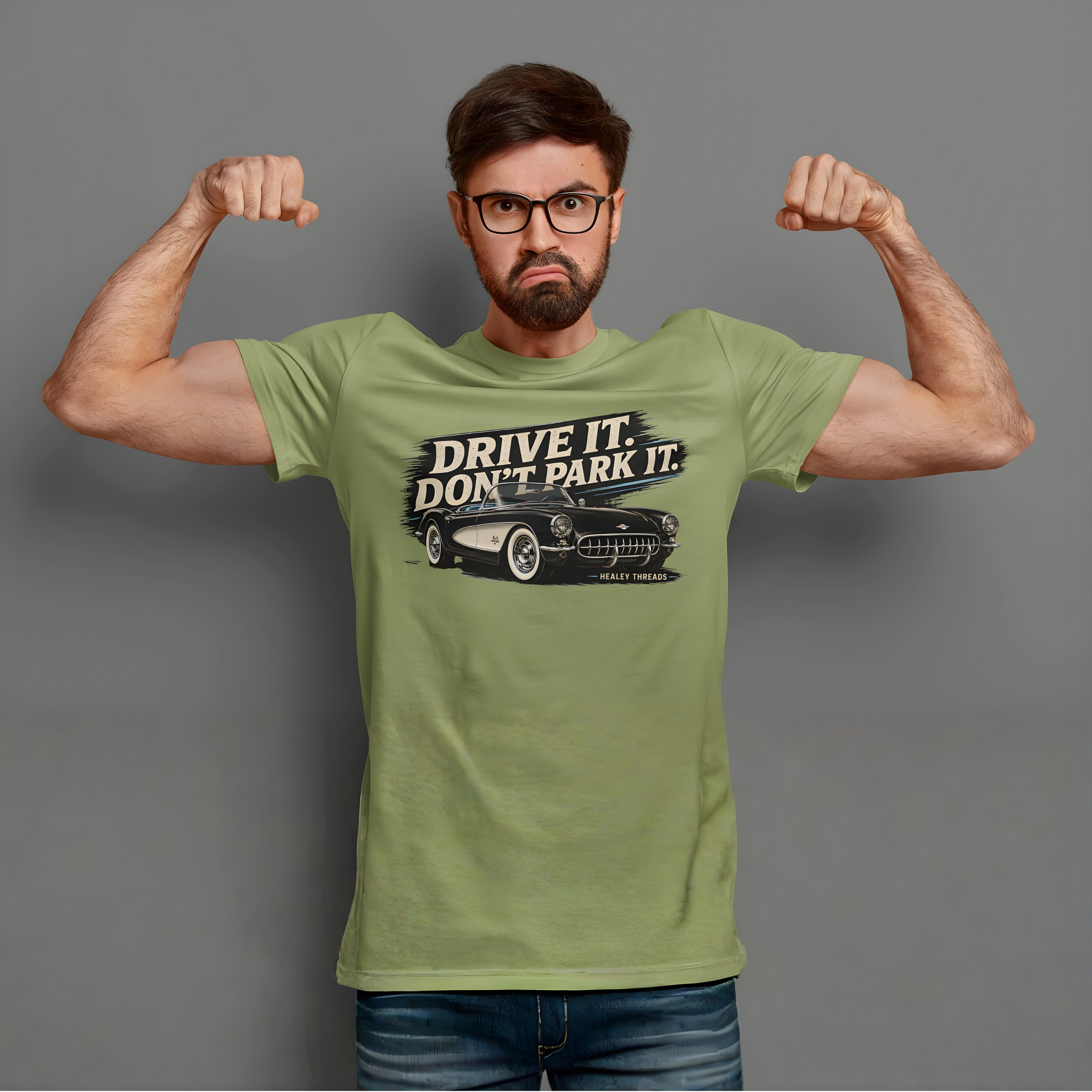 Man wearing a military green t-shirt with a vintage car graphic and text, flexing his muscles against a gray background