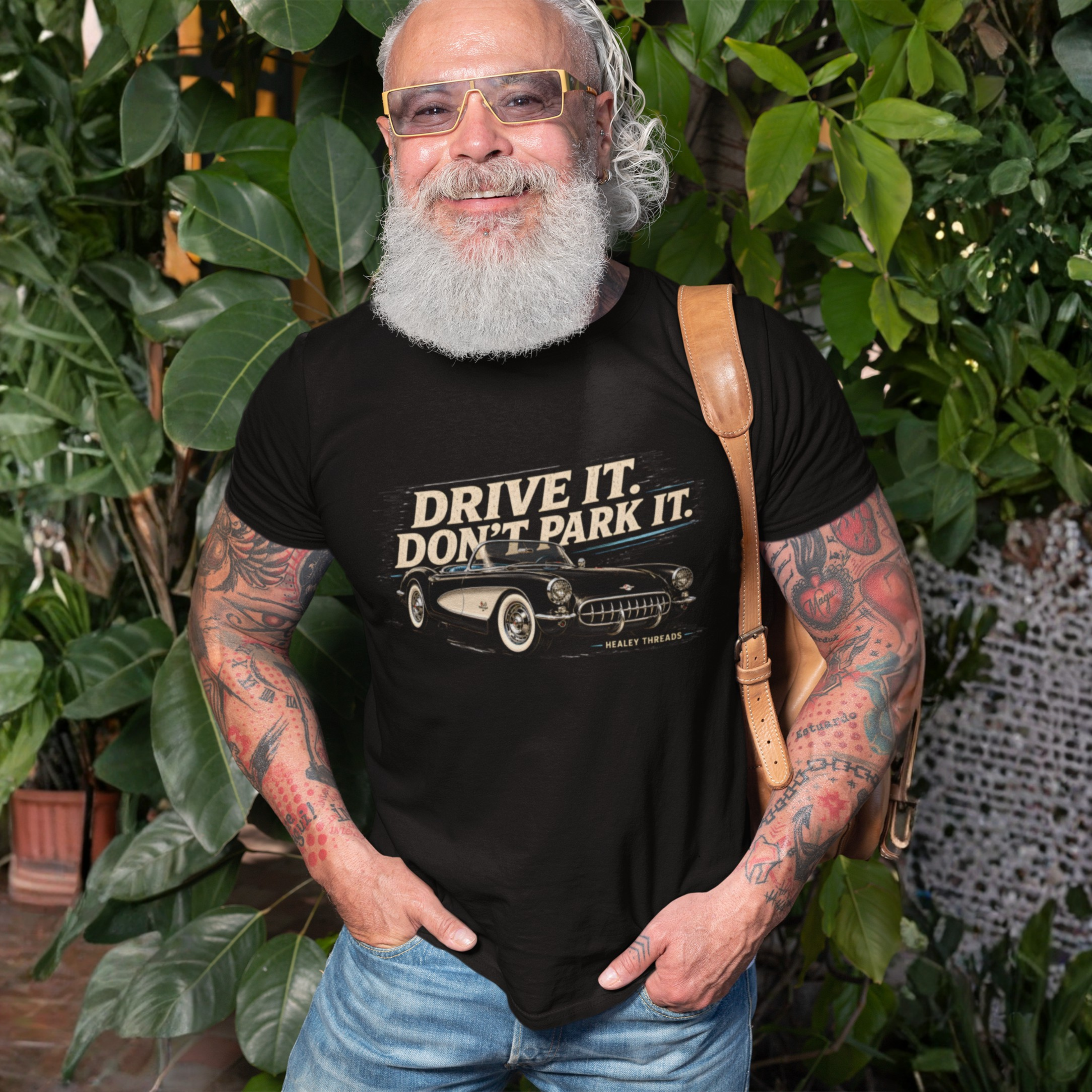 Man wearing a black t-shirt with 'Drive It. Don't Park It.' text and graphic vintage car, standing outdoors with greenery.