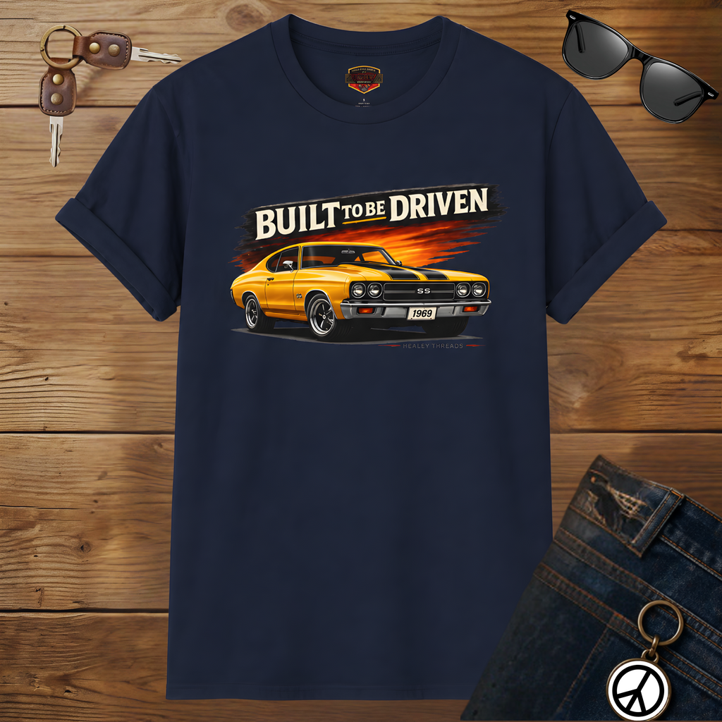 Navy blue t-shirt with a yellow car graphic and 'Built to be Driven' text on a wooden surface.