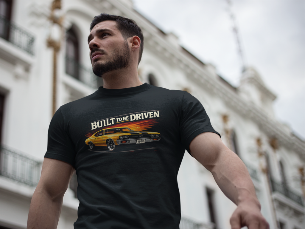 Man wearing a black t-shirt with a car built to be driven graphic and text, standing in front of a building.