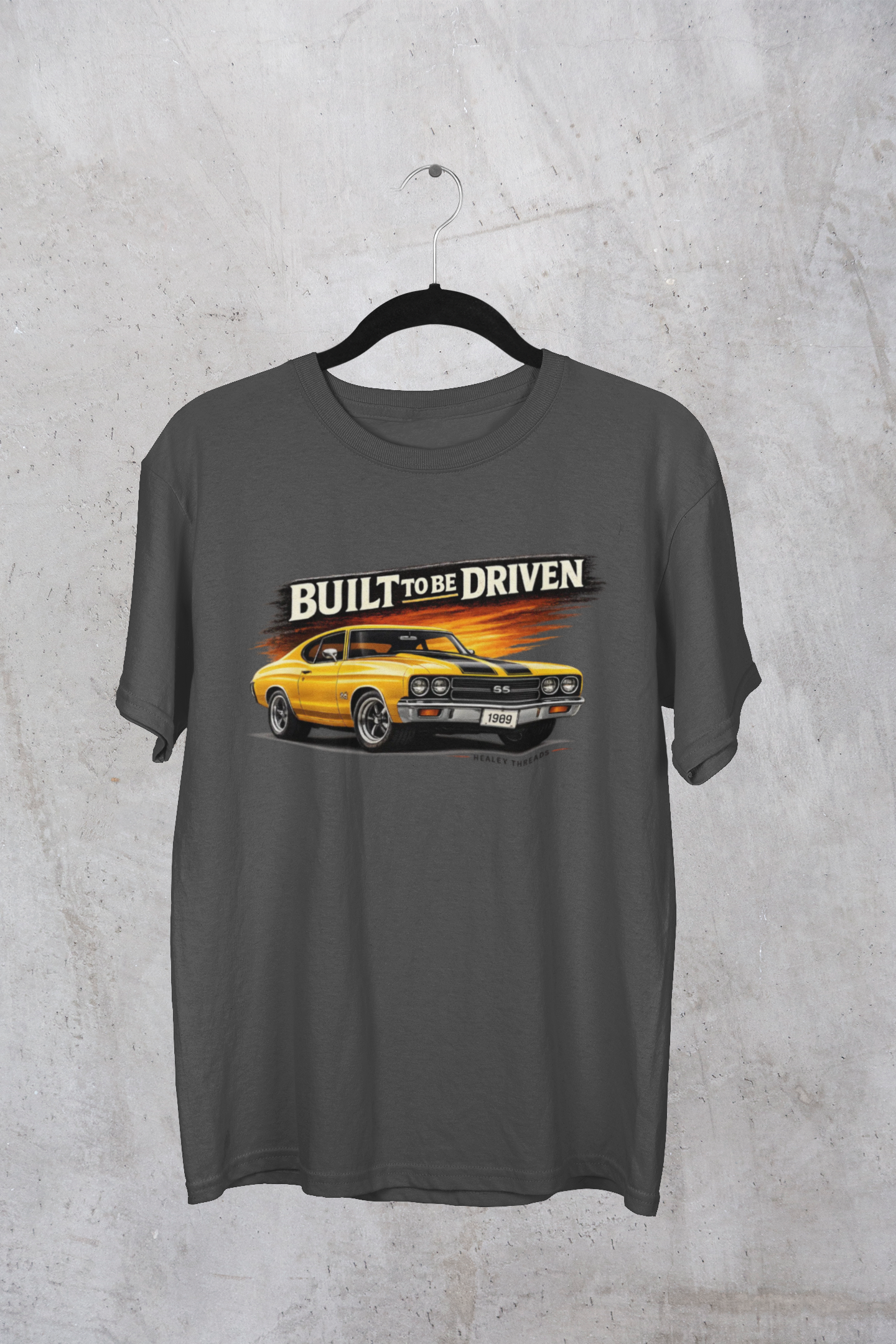 Dark heather t-shirt with a yellow car graphic and 'Built to be Driven' text on a textured gray background